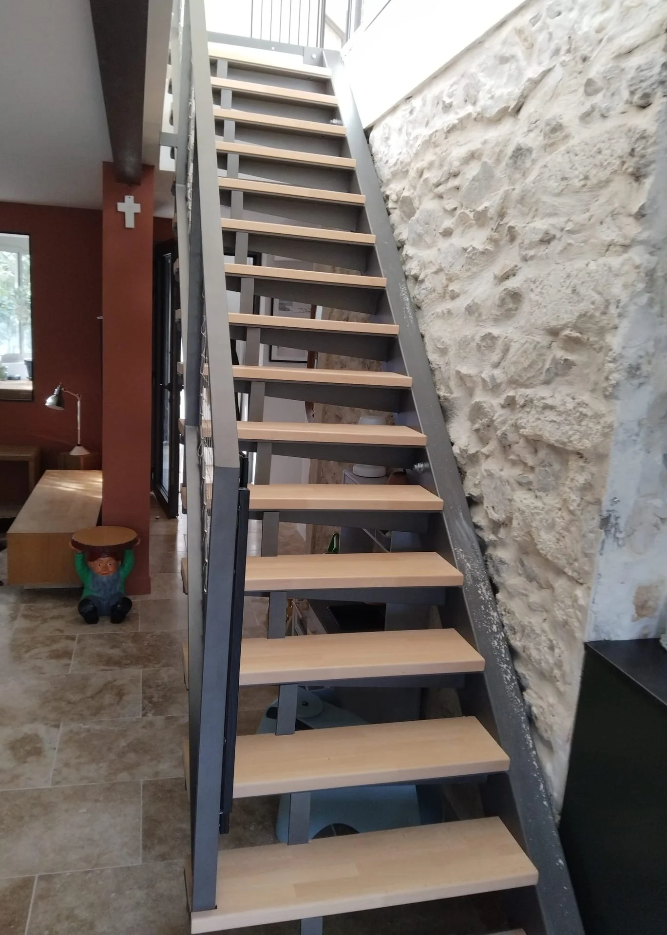 Escalier droit sur mesure, limons en acier anthracite et marches en bois clair le long d’un mur en pierre