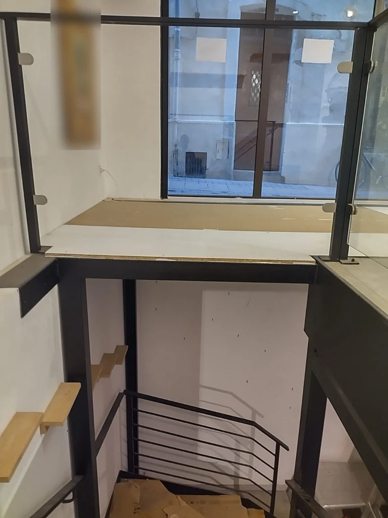 Mezzanine en acier d’un local commercial, garde-corps en verre à pinces sur poteaux acier