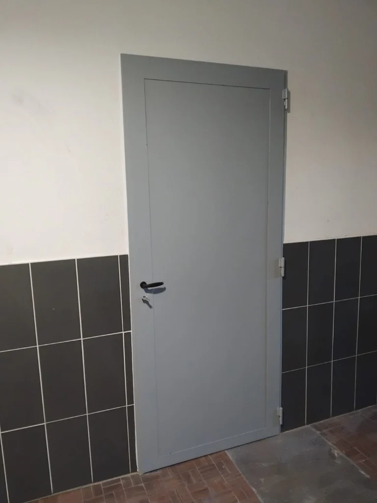 Porte pleine en acier gris posée dans un couloir carrelé